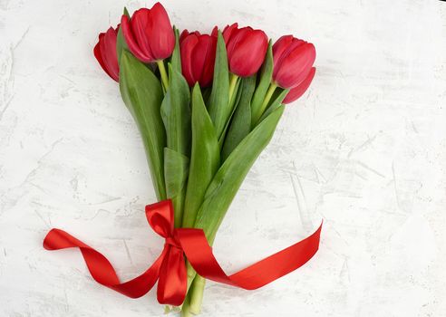 bouquet of red blooming tulips with green stems and leaves on a white cement background. Festive backdrop for birthday, Valentine's day, anniversary