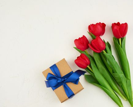 bouquet of red blooming tulips with green leaves, wrapped gift in brown craft paper on a white background, copy space. Festive backdrop for birthday, Valentine's day