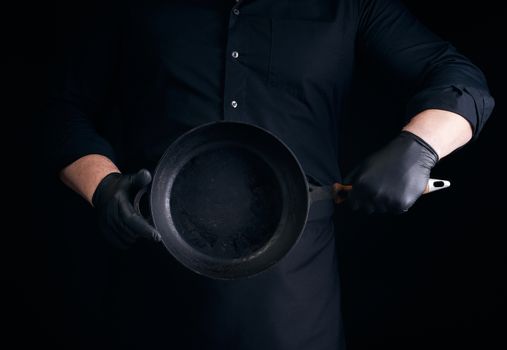 male cook in black uniform and latex gloves holds an empty round vintage black cast iron pan in front of him, low key