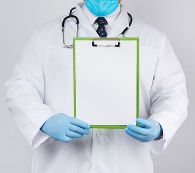 male doctor in a white medical coat and blue latex gloves holds a tablet with a paper clip with a white blank sheet, place for an inscription