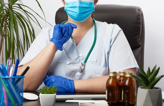 doctor in uniform and blue latex gloves sits at a work table in his office, concept of patient reception in the clinic