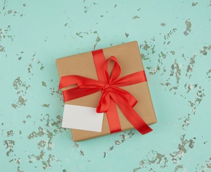 square box wrapped in brown kraft paper and tied with a red silk ribbon, on top of an empty white business card, green background
