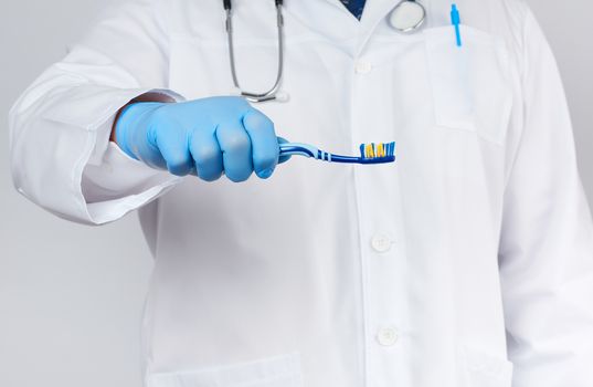 adult doctor therapist is dressed in a white robe uniform and blue sterile gloves is standing and holding a toothbrush, daily brushing concept, white background