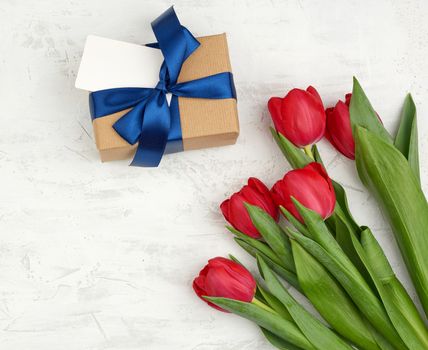 bouquet of red blooming tulips with green leaves, wrapped gift in brown craft paper on a white background, copy space. Festive backdrop for birthday, Valentine's day