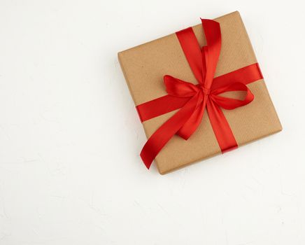square box wrapped in brown kraft paper and tied with a red silk ribbon, white background, top view