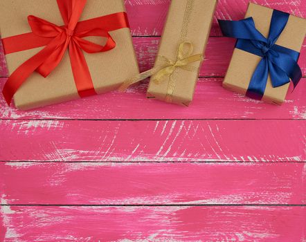 gifts wrapped in brown kraft paper and a silk ribbon, pink wooden background. festive backdrop for birthday and valentines day