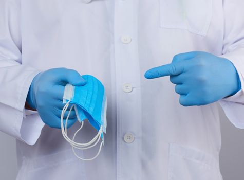 doctor in a white coat, blue latex sterile gloves holds textile medical masks in his hand, protective accessory against viruses and bacteria, close up