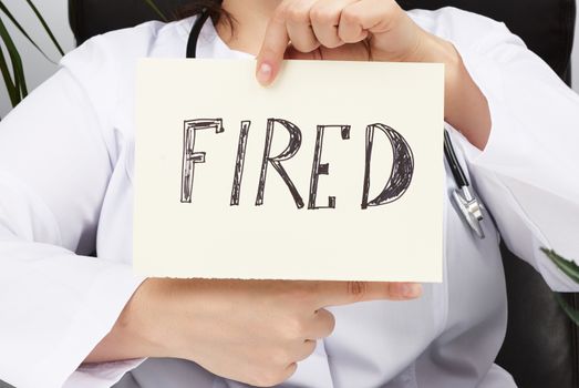 medic in a white coat holds a sheet of paper with the inscription fired and points his right hand with the index finger to the right, concept of job loss
