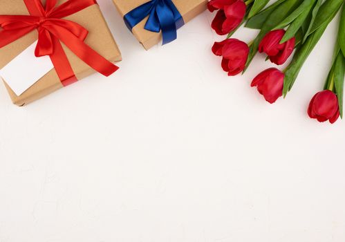bouquet of red blooming tulips with green leaves, wrapped gift in brown craft paper on a white background, copy space. Festive backdrop for birthday, Valentine's day