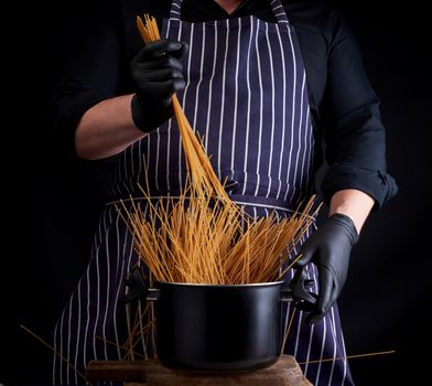 uncooked yellow long spaghetti in a black metal pan and a chef in a striped apron, cooking process