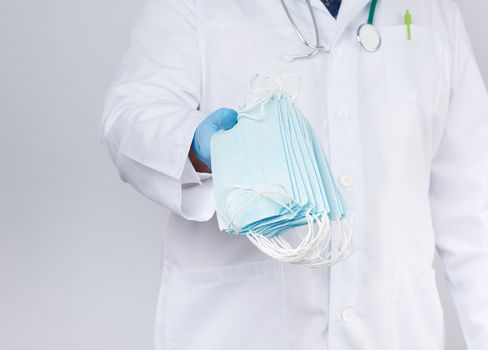 doctor in a white coat, blue latex sterile gloves holds textile medical masks in his hand, protective accessory against viruses and bacteria, close up