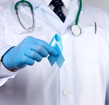 doctor in a white coat and tie stands and holds a blue silk ribbon in a loop, wearing blue sterile medical gloves, symbol of the fight and treatment of prostate cancer