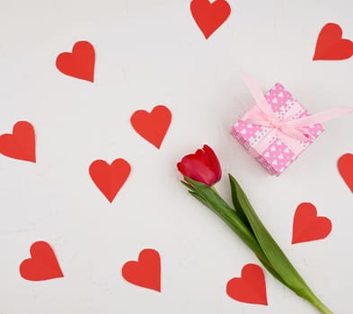 bouquet of red blooming tulips with green stems and leaves and red paper heart on a white cement background. Festive backdrop for birthday, Valentine's day