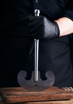 man in black clothes, latex gloves holds a vintage metal ax-knife for meat and vegetables, dark background