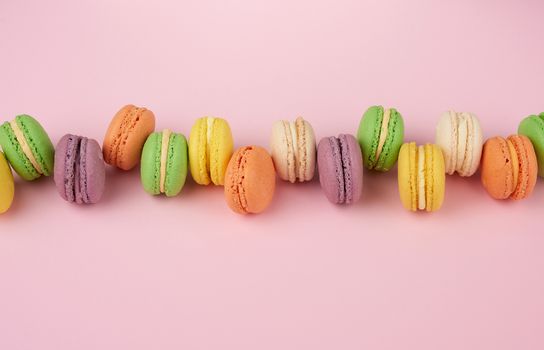 many multi-colored round baked macarons cakes on a light pink background, top view