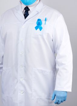 male doctor in a white coat and tie stands and holds a blue silk ribbon in a loop, wearing blue sterile medical gloves, symbol of the fight and treatment of prostate cancer