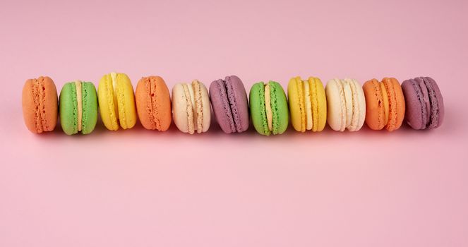 many multi-colored round baked macarons cakes on a light pink background, top view