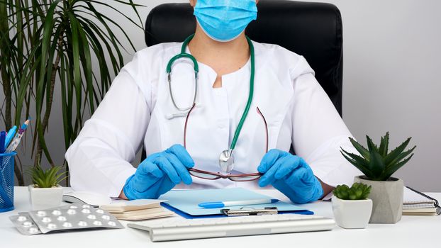 woman doctor in a white coat, sterile medical gloves writes a prescription on a form, therapist sits on a chair at a white table