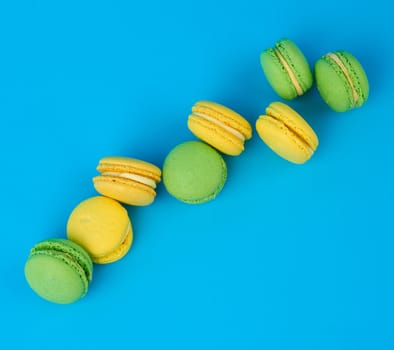 stack of yellow and green round almond flour cakes macarons with cream on a blue background, delicious pastry, top view