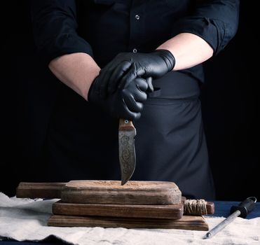 male cook in black uniform and black latex gloves holds a vintage sharp knife over a cutting board, black background