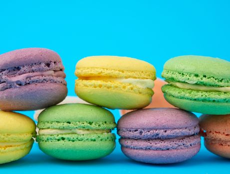 multi-colored round baked macarons cakes on a light blue background, close up