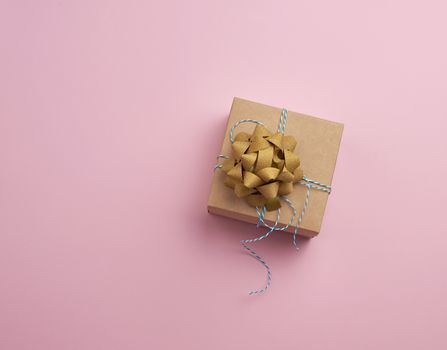 closed brown square box with a gift tied rope on a pink background, top view, empty place for an inscription