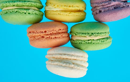 stack of multi-colored round baked macarons cakes on a blue background, close up