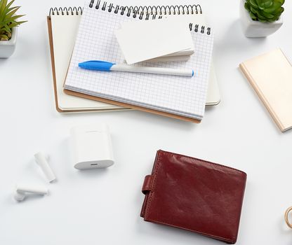 notebooks, pen, stack of business cards, brown leather wallet and power bank with a cord on a white table, workplace, top view