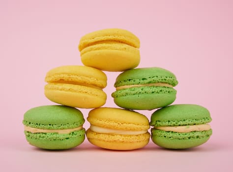 stack of yellow and green round almond flour cakes macarons with cream on a pink background, delicious cake