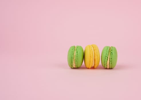 green and yellow round baked macarons on a pink background, delicious popular french dessert