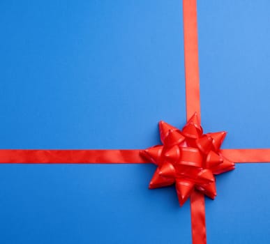 red silk ribbon crossed on a  blue background in the middle of a red bow, imitation of tying a gift, top view