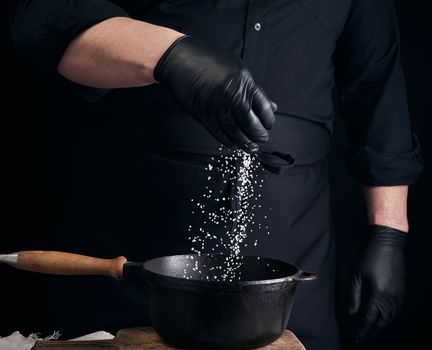 male cook in black uniform and latex gloves salt food in a black cast-iron pan, salt crystals froze in the air, low key