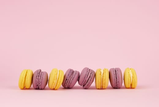 many multi-colored round baked macarons cakes on a light pink background, close up, copy space