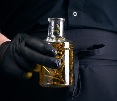 man in black clothes, latex gloves holds a transparent bottle with olive oil, low key, close up