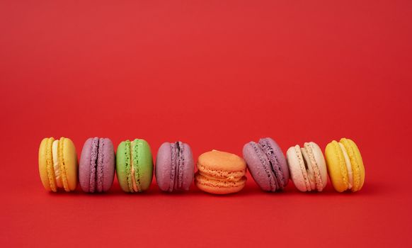 pile of multi-colored baked macarons almond flour cakes on a red background, copy space