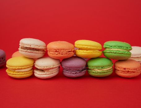 pile of multi-colored baked macarons almond flour cakes on a red background, close up