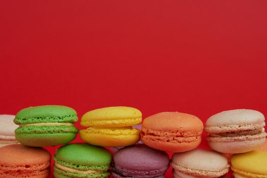 pile of multi-colored baked macarons almond flour cakes on a red background, copy space