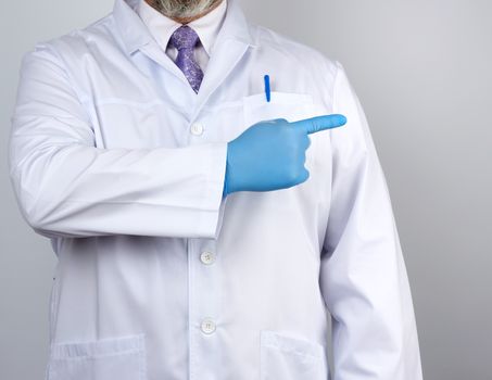 medic man in white coat with buttons, on hands wearing blue sterile gloves, showing hand gesture indicating the subject, white background