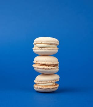 stack of white round baked almond flour cakes macarons on a dark blue background, delicious popular french dessert, close up