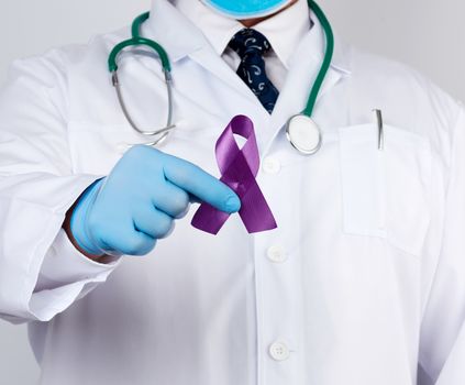 male doctor in a white coat and tie stands and holds a purple silk ribbon in the form of a loop, wearing blue sterile medical gloves. Symbol of early research and disease control, Alzheimer's disease