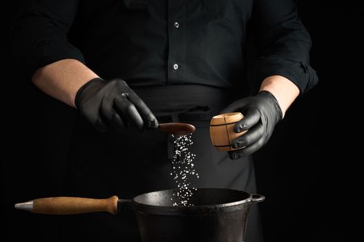 male cook in black uniform and latex gloves salt food in a black cast-iron pan, salt crystals froze in the air, low key