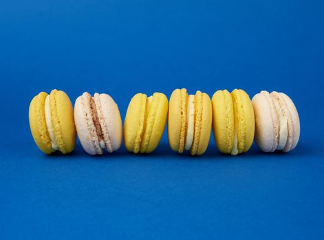 stack of multi-colored round baked macarons cakes on a dark blue background, dessert lies in a row, close up