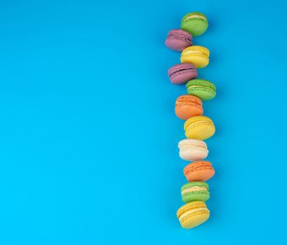 round multi-colored baked macarons with cream lie in a line on a blue background, flat lay, copy space