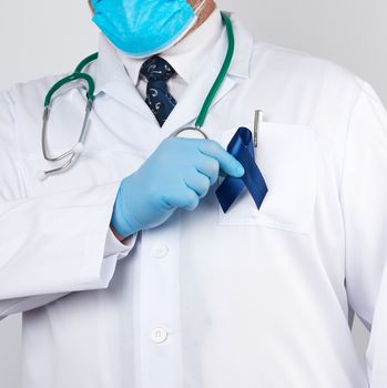 doctor in white uniform and sterile latex gloves holds a dark blue ribbon, concept of timely research and disease prevention colon malignancies, chronic fatigue syndrome, tuberous sclerosis