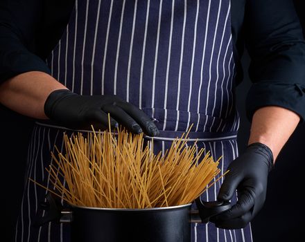 uncooked yellow long spaghetti in a black metal pan and a chef in a striped apron, cooking process