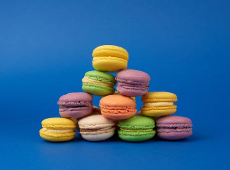 stack of multi-colored round baked macarons cakes on a dark blue background, dessert stands in a row