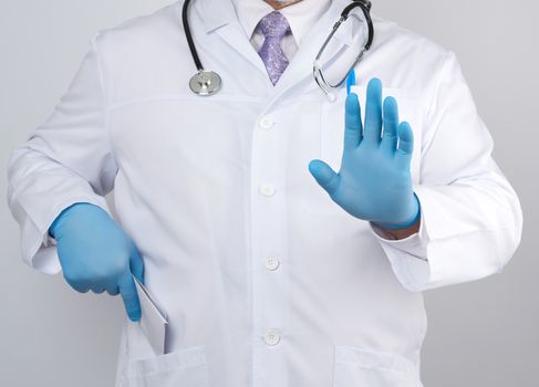 male doctor in a white coat and blue sterile gloves shows a stop gesture with his hand, white background