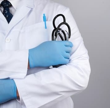 adult male doctor in a white medical coat stands and holds a black stethoscope on a white background, close up