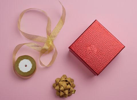 square red box tied with a golden ribbon, concept of congratulations and gifts, top view, pink background
