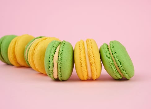 green and yellow round baked macarons on a pink background, delicious popular french dessert